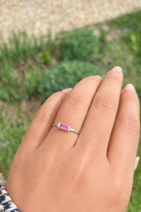 Hand wearing a ring with a Padparadascha gemstone against a blurred green background
