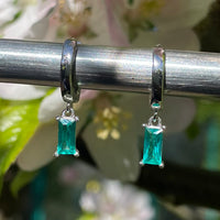 Silver earrings with green gemstones on a metal rod against a floral background