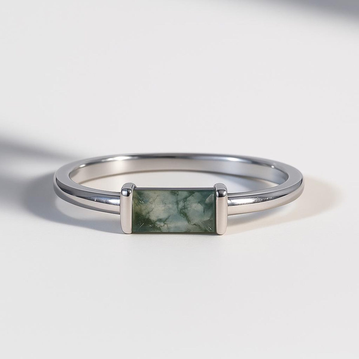 Silver ring with a rectangular moss agate stone on a light gray background