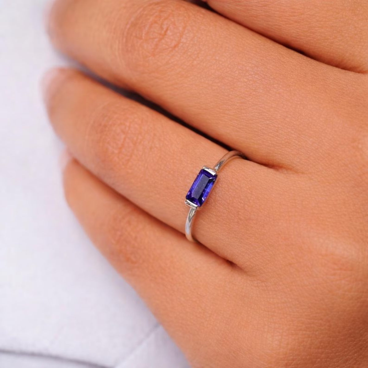 Silver ring with a blue gemstone on a hand against a white background