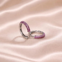 Pair of silver hoop earrings with pink gemstones on a pink satin background