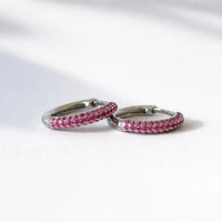 Pair of silver hoop earrings with pink gemstones on a white background