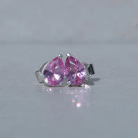 Pair of silver earrings with pink teardrop-shaped gemstones on a light gray background