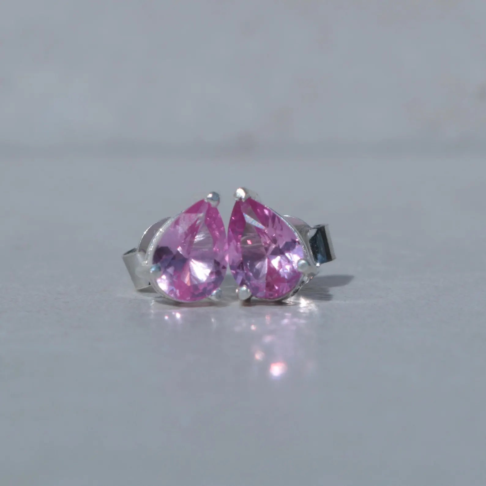 Pair of silver earrings with pink teardrop-shaped gemstones on a light gray background
