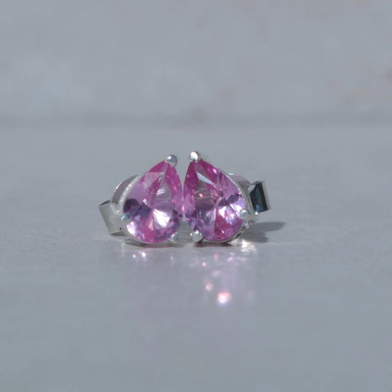 Pair of silver earrings with pink teardrop-shaped gemstones on a light gray background