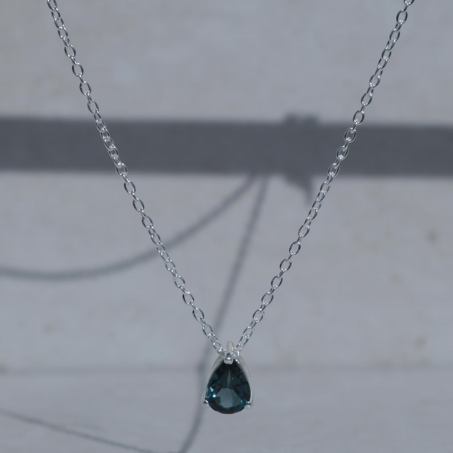 Necklace with a teardrop-shaped blue gemstone pendant on a light gray background