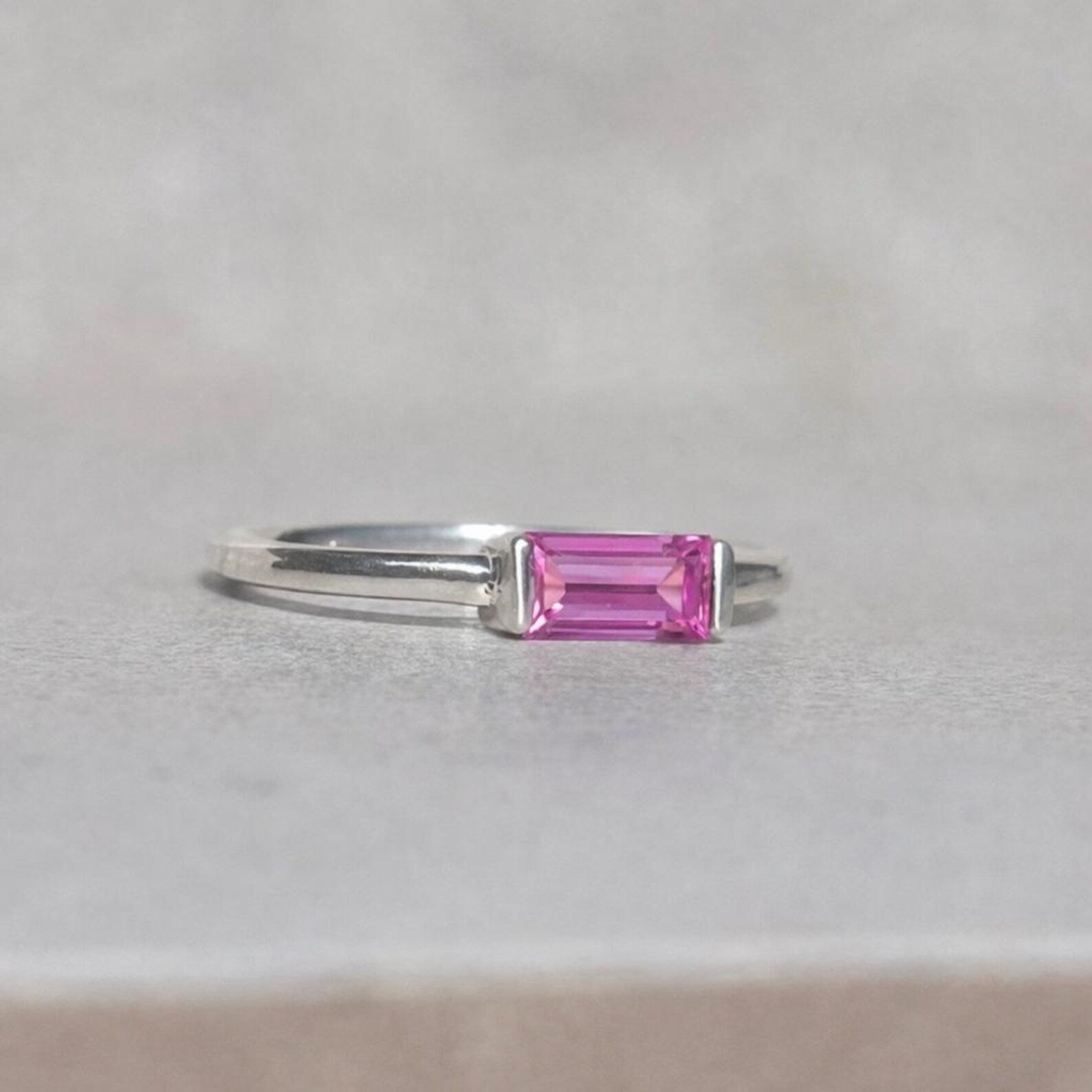 Silver ring with a pink sapphire gemstone on a light grey background