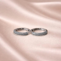 Pair of silver aquamarine hoop earrings with embedded stones on a pink satin background