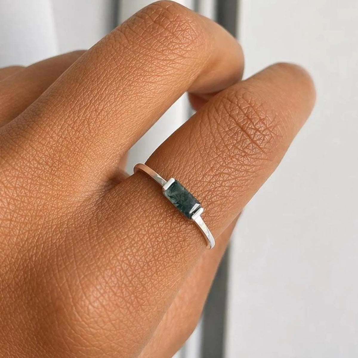 Silver ring with a moss agate stone on a person's finger against a neutral background