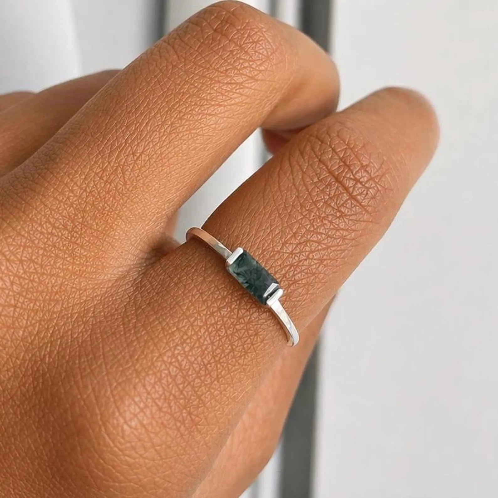 Silver ring with a moss agate stone on a person's finger against a neutral background