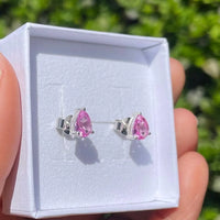 Pink teardrop earrings in a white jewelry box held by a hand with a blurred green background