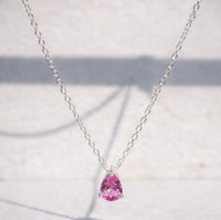 Pink sapphire teardrop pendant on a silver chain against a light background