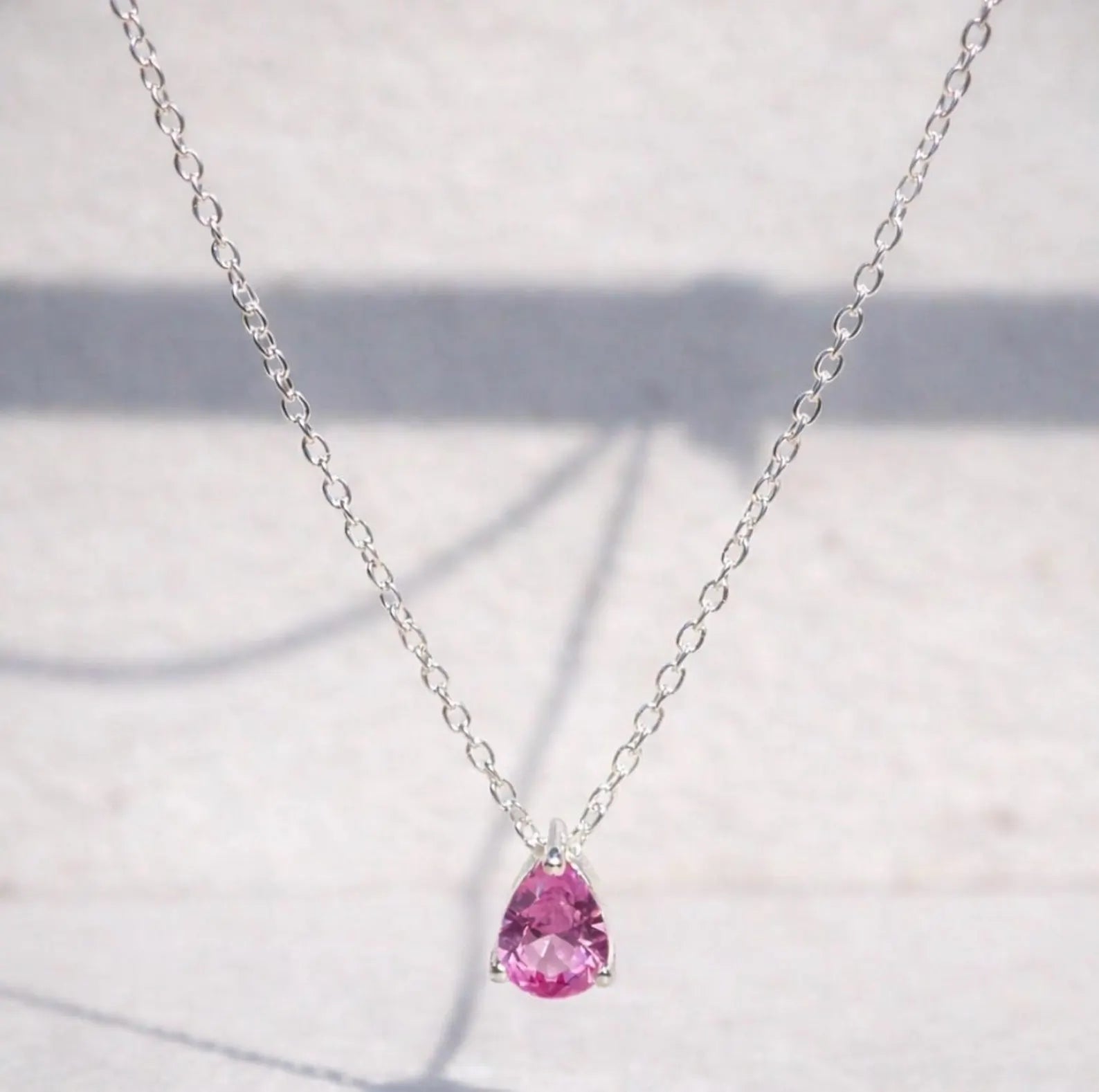 Pink sapphire teardrop pendant on a silver chain against a light background