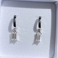 Pair of silver hoop earrings with baguette cut gemstones in a white box.