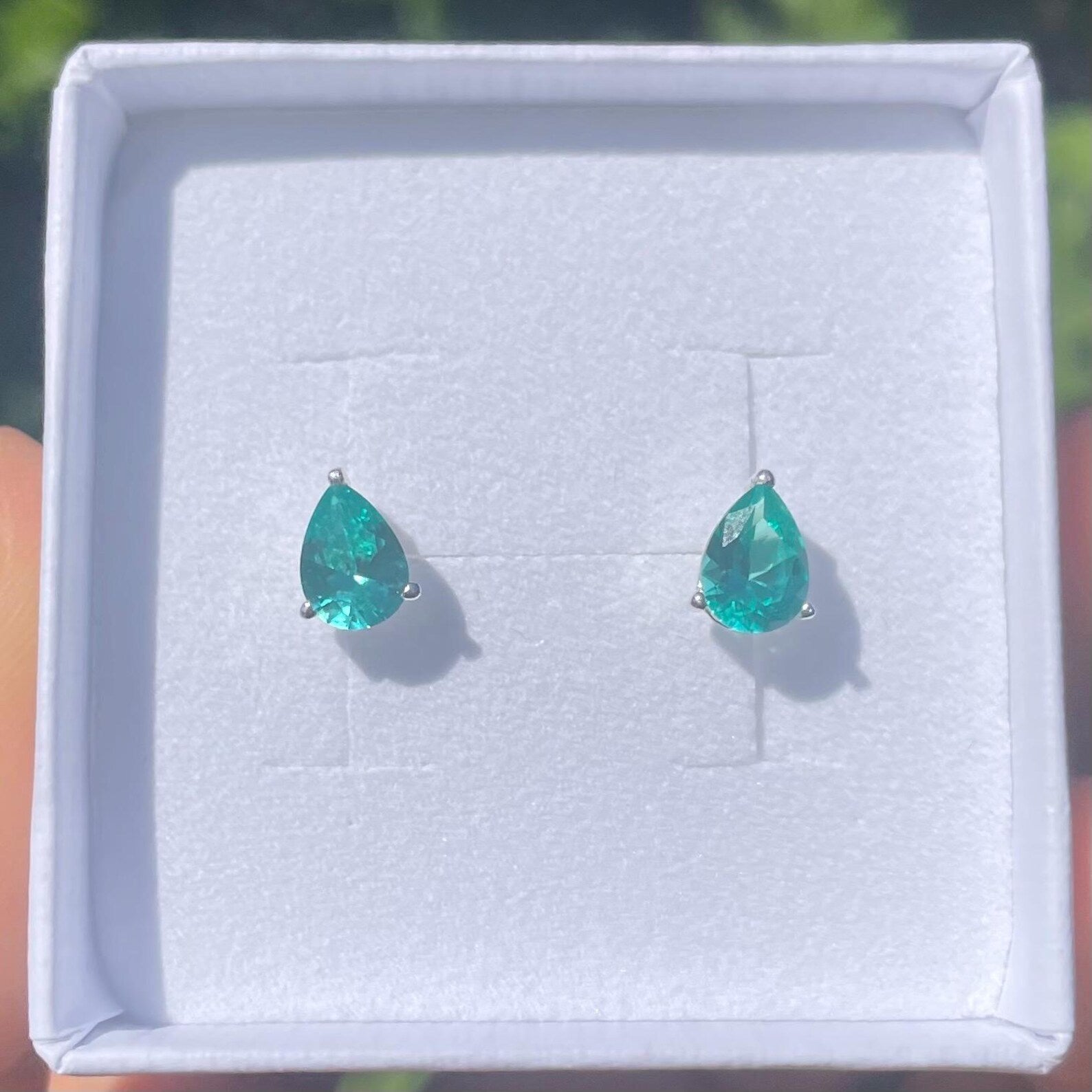 Teardrop-shaped green gemstone earrings in a white jewellry box.