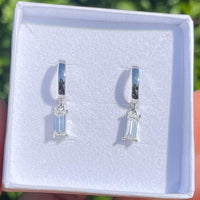 Pair of silver earrings with gemstones in a white box against a green outdoor background