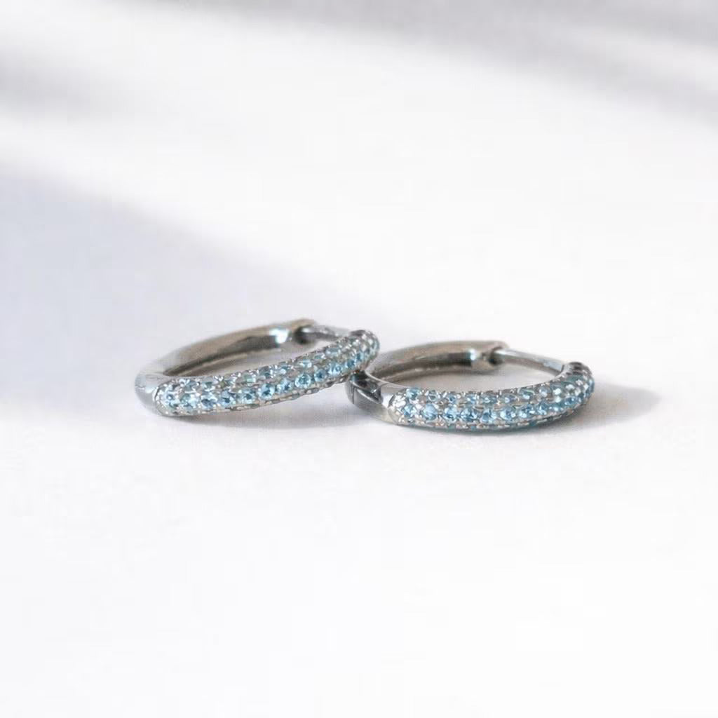 Pair of silver aquamarine hoop earrings with blue gemstones on a white background
