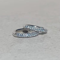 Pair of silver aquamarine hoop earrings with clear gemstones on a light gray background