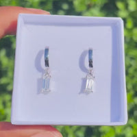Silver hoop earrings with baguette-cut gemstones in a white jewelry box.